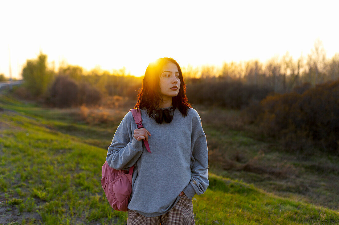 Woman wearing grey sweatshirt standing in meadow at sunset \n