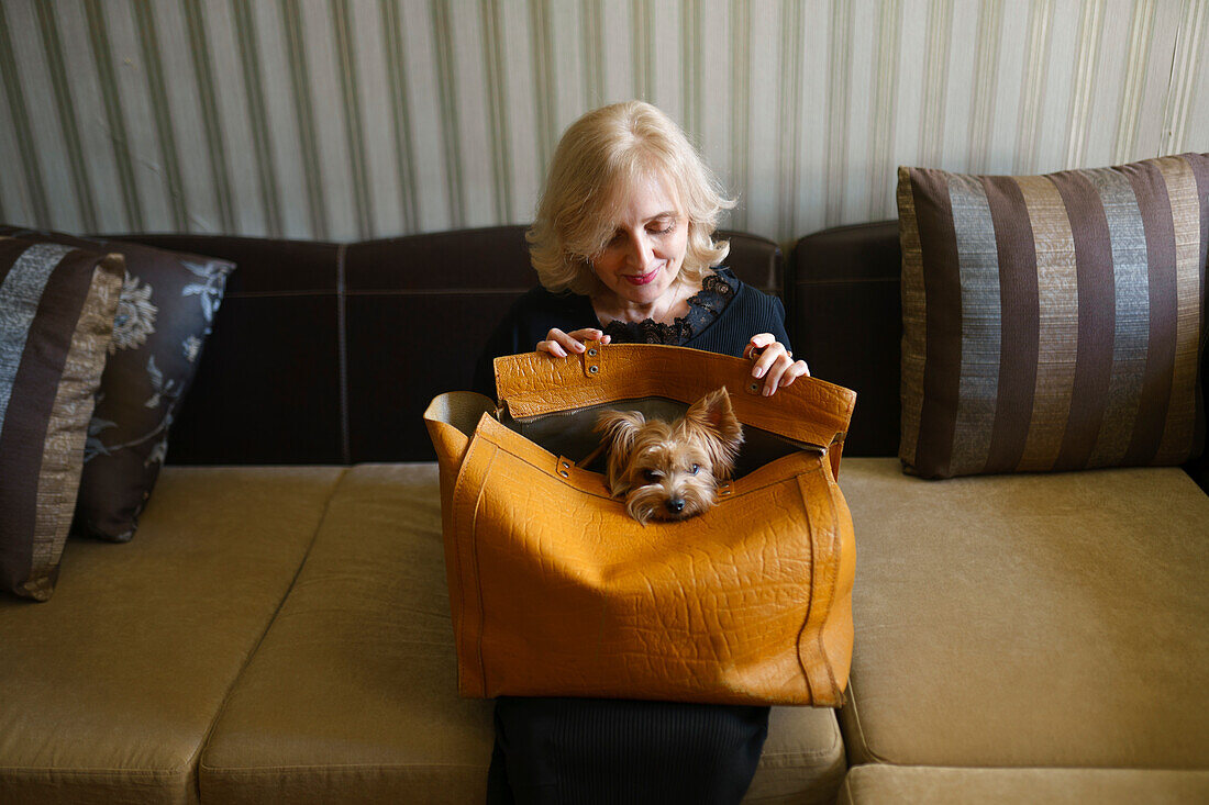 Frau mit Yorkshire-Terrier auf dem Schoß, Tasche im Wohnzimmer