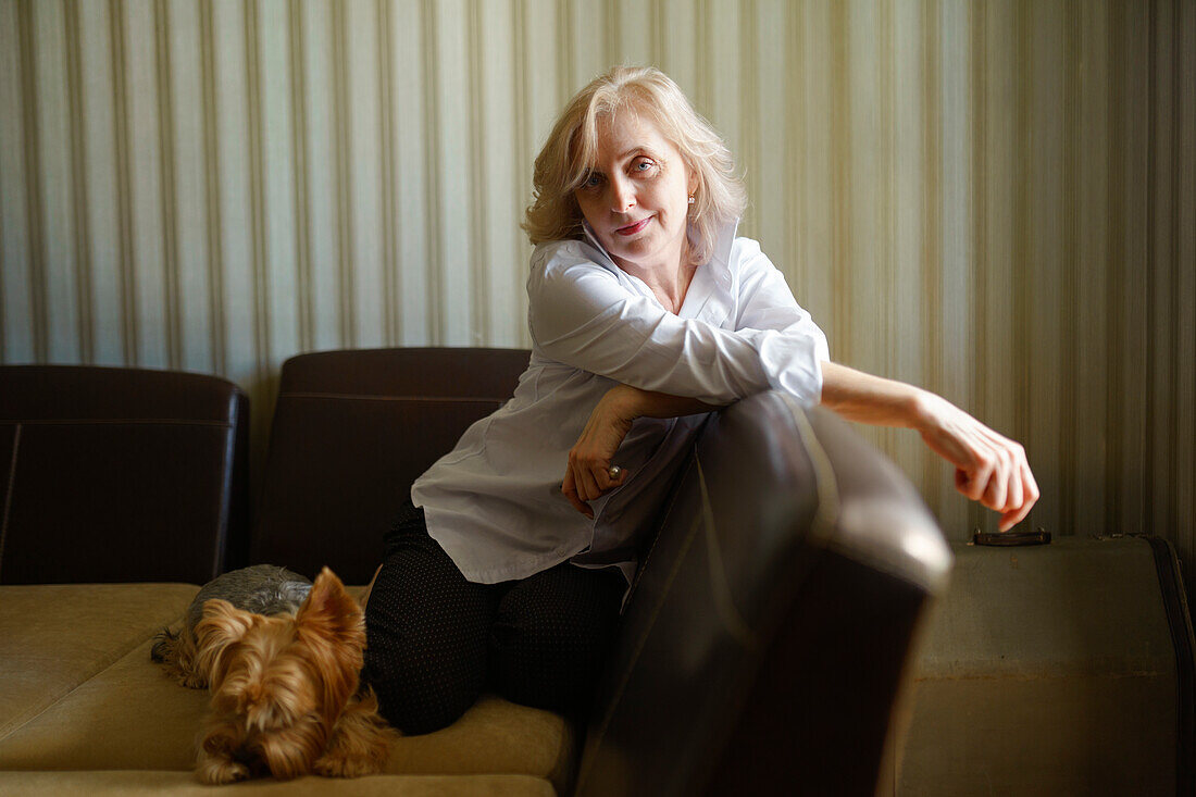 Woman leaning on sofa next to Yorkshire terrier in living room \n