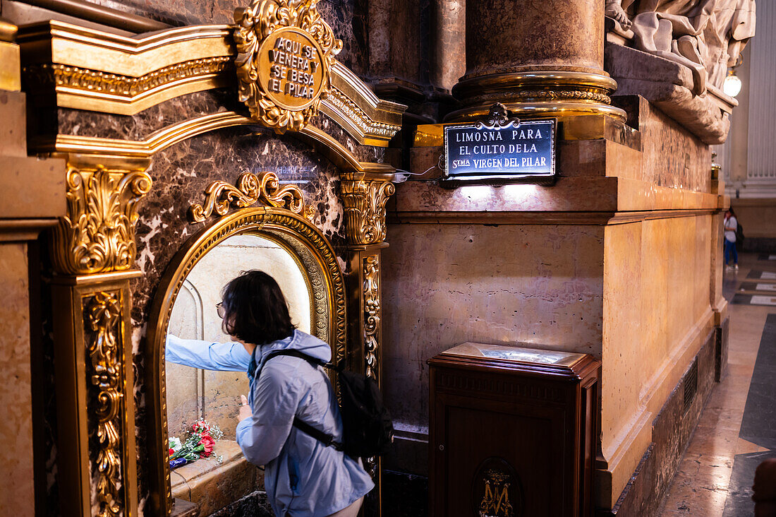 Asiatische Gläubige küssen die Säule in der Kathedrale-Basilika Unserer Lieben Frau von der Säule während des Blumenopfers für die Virgen del Pilar, der wichtigsten und beliebtesten Veranstaltung der Fiestas del Pilar, die am Tag der Spanier stattfindet, Zaragoza, Spanien