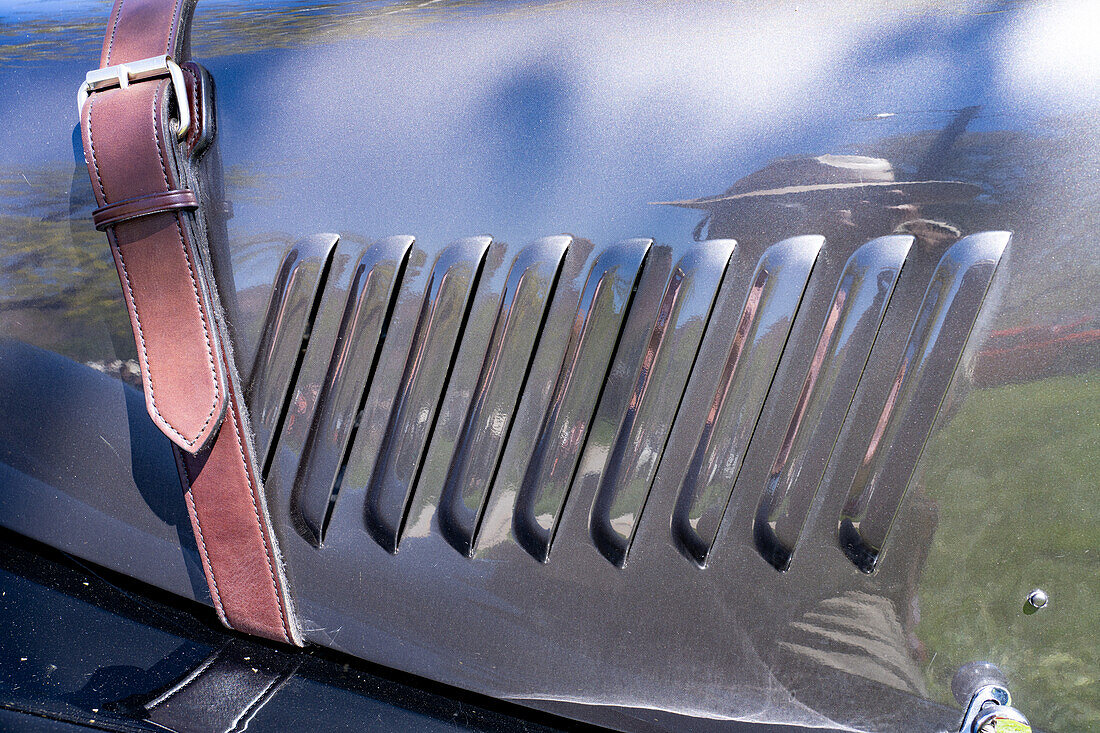 Leather strap and louvers on the hood or bonnet of a 1991 Morgan Plus 8 sports car in a car show in Moab, Utah.\n