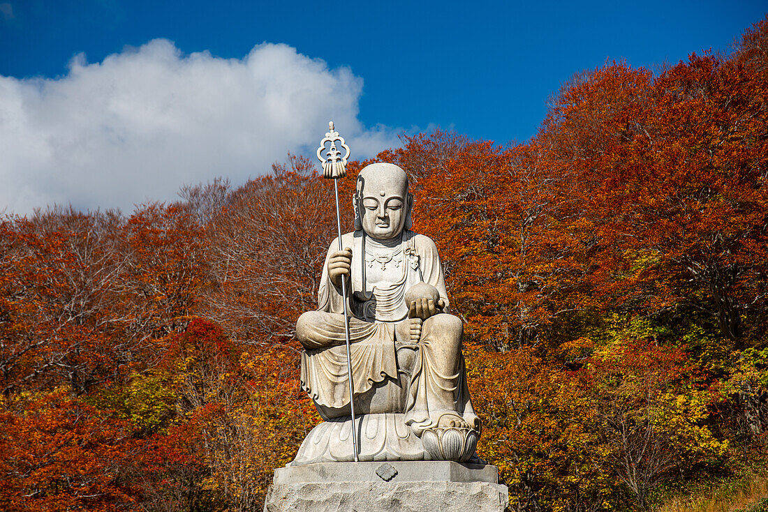 Große Shizo-Statue vor feuerrotem Herbstlaub in einem schönen japanischen Tempel inmitten von Herbstfarben, Osorezan Bodaiji-Tempel, Mutsu, Aomori-Präfektur, Honshu, Japan, Asien