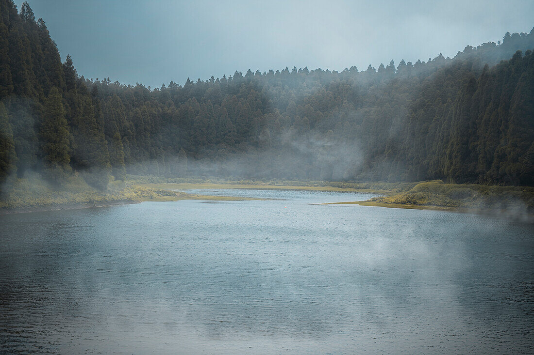 Lagoa do Eguas lake framed by a forest in a cloudy day with some low fog, Azores islands, Sao Miguel island, Portugal, Atlantic, Europe\n