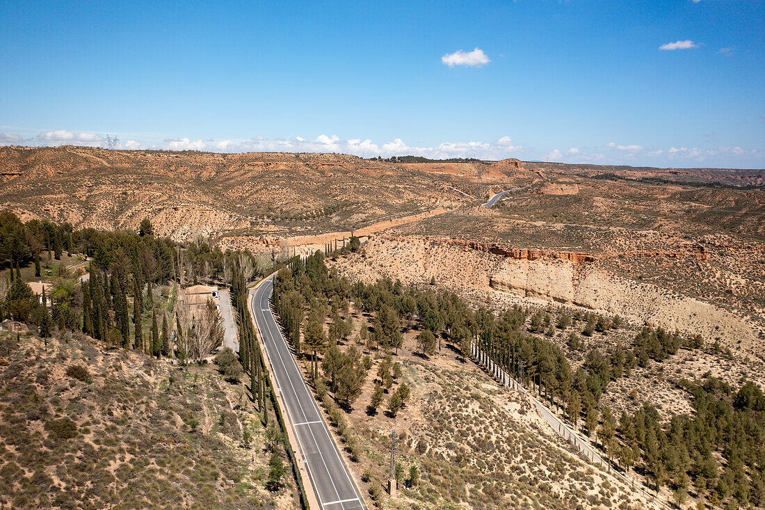 Drohnenaufnahme einer Straße durch eine wüstenähnliche Landschaft in der Nähe des Francisco Abellan-Staudamms und -Stausees, Granada, Andalusien, Spanien, Europa