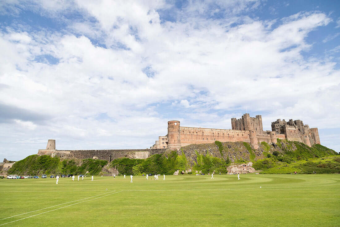 Bamburgh Castle, a medieval fortress, Grade I Listed Building constructed on top of a craggy outcrop of volcanic dolerite, overlooking a cricket ground, Bamburgh, Northumberland, England, United Kingdom, Europe\n