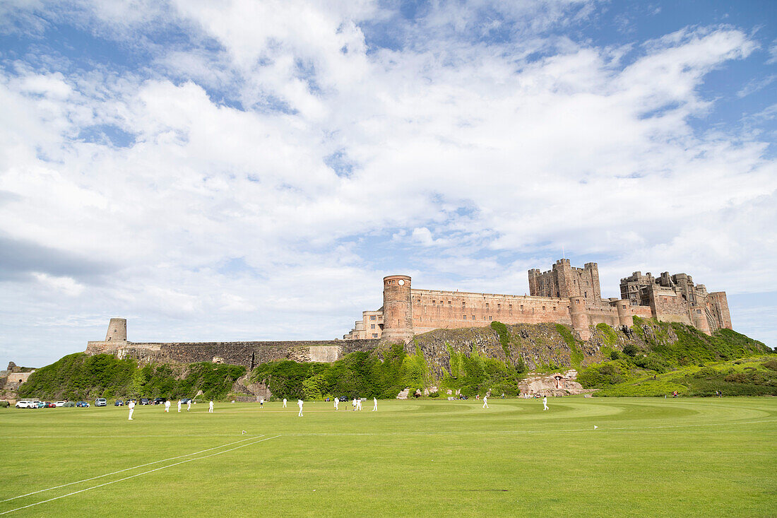 Bamburgh Castle, eine mittelalterliche Festung, denkmalgeschütztes Gebäude, errichtet auf einem zerklüfteten Felsvorsprung aus vulkanischem Dolerit, mit Blick auf einen Cricketplatz, Bamburgh, Northumberland, England, Vereinigtes Königreich, Europa