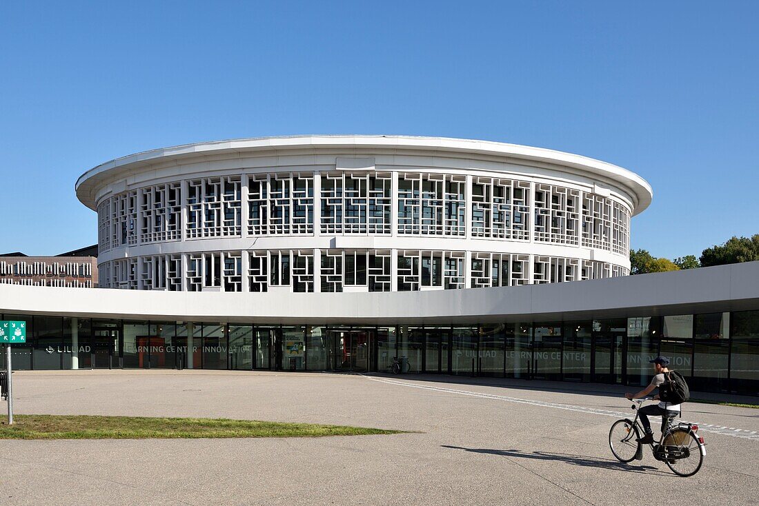 Frankreich, Nord, Villeneuve d'Ascq, Universität Lille, Campus der Cité Scientifique, kreisförmiges Gebäude, das die Bibliothek beherbergt und LILLIAD (Learning Center Innovation1) genannt wird, ein wissenschaftliches Zentrum der Universität Lille (wissenschaftliche Universitätsbibliothek, Multimedia, große wissenschaftliche Sammlung, erweiterte Bibliothek und digitalisierte Ressourcen), radfahrender Student