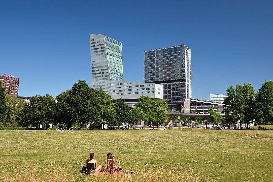 France, Nord, Lille, Henri Matisse park with the Euralille business district which includes the Eurostar station and the Lille Europe TGV station, dominated by the Lille tower and the Lilleurope tower, two young women seated in the grass\n