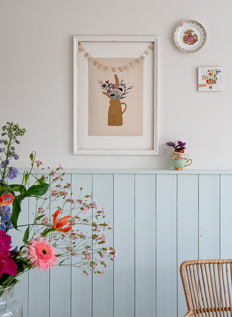 Floral picture and garland over pastel-colored wood paneling in the living room