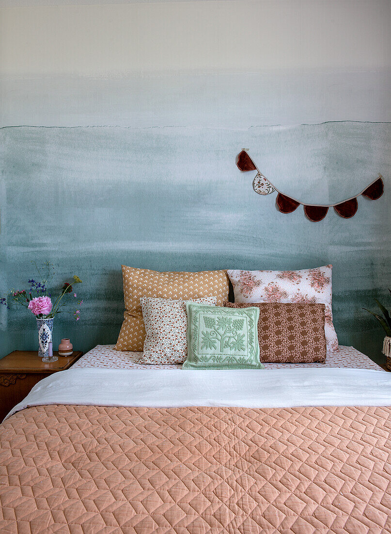 Doppelbett mit gemusterten Kissen vor bemalter Wand mit Ozeanmotiv