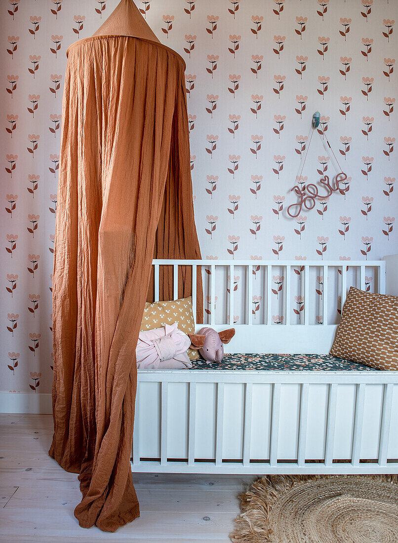 Cot with orange canopy in the nursery with floral wallpaper