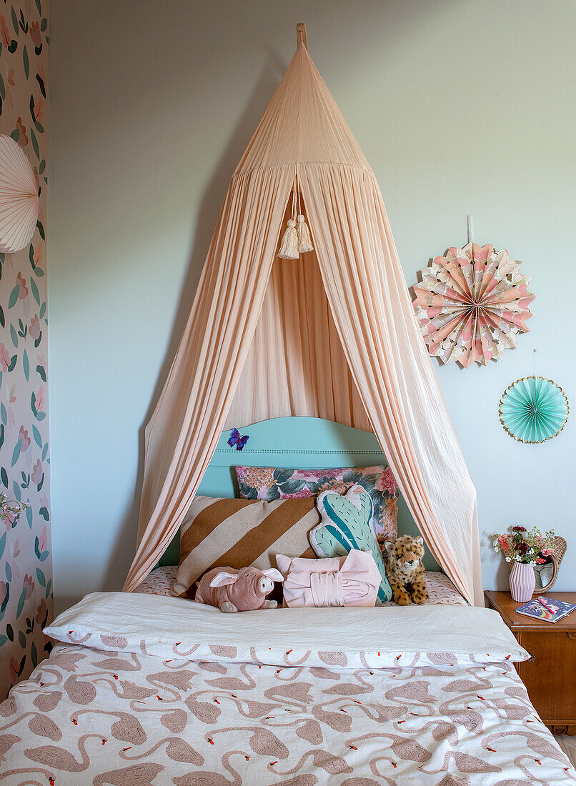 Bed with peach-colored canopy, fun throw pillows and cuddly toys in a nursery