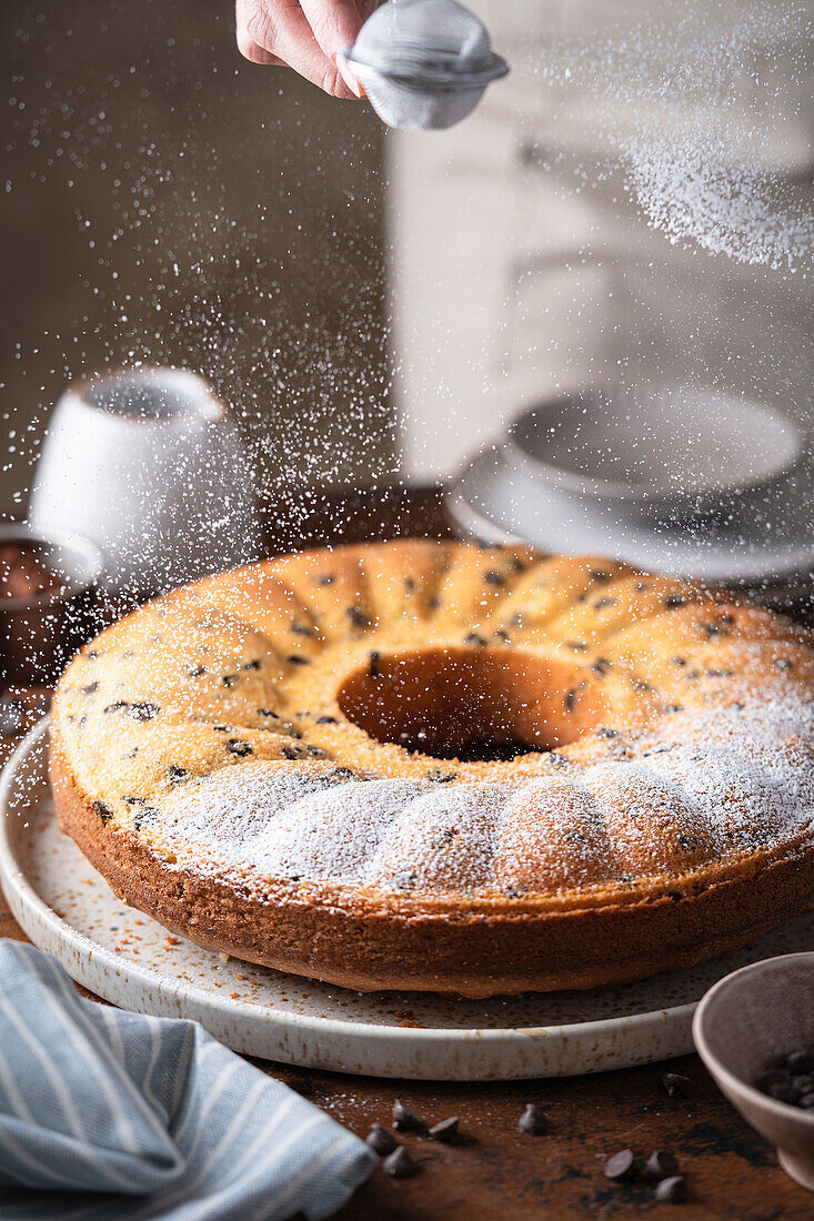 Vanillegugelhupf mit Schokostückchen mit Puderzucker bestäuben