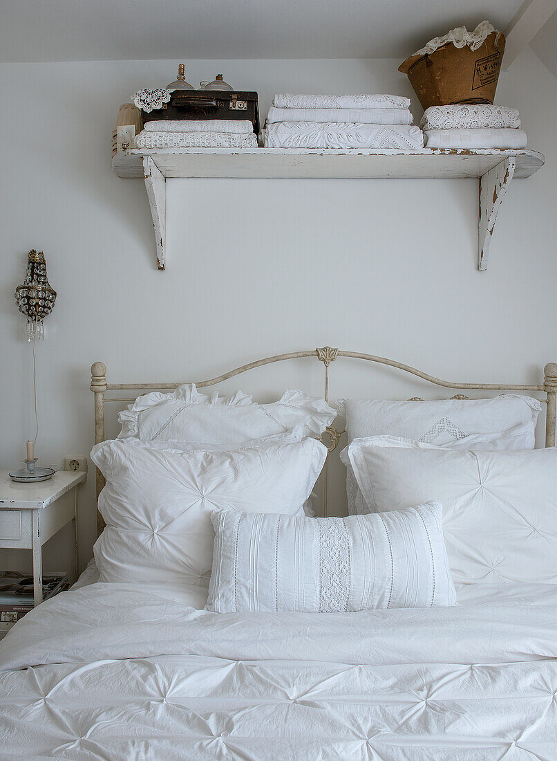 White, romantic bedroom with ornate iron bed and wall shelf