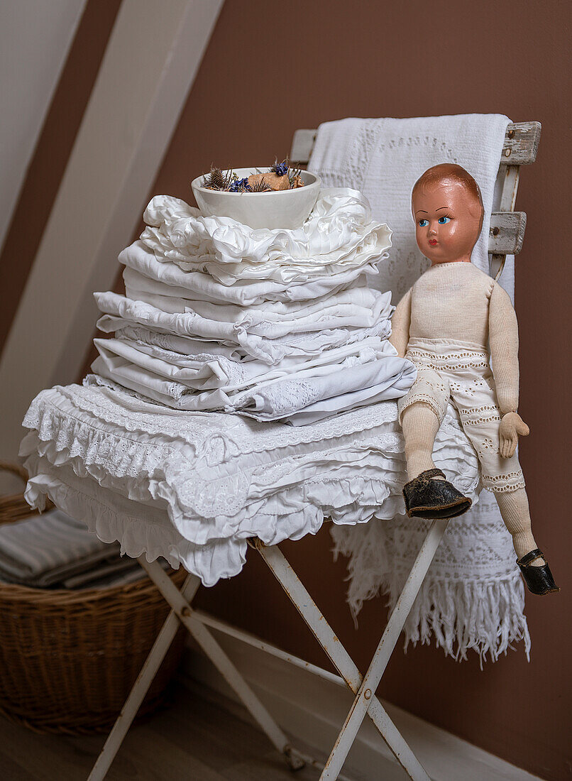 White pile of linens and vintage doll on wooden chair