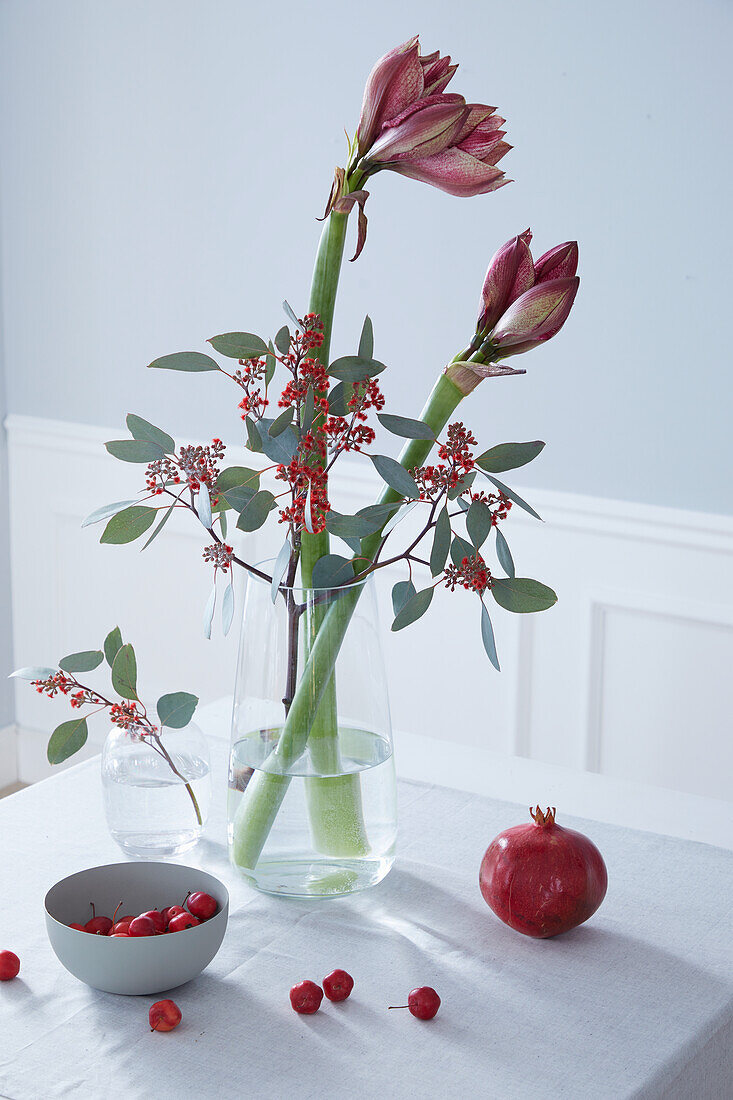 Rot schimmernde Amaryllis, rot blühender Eukalyptus, Granatapfel und kleine rote Holzäpfel