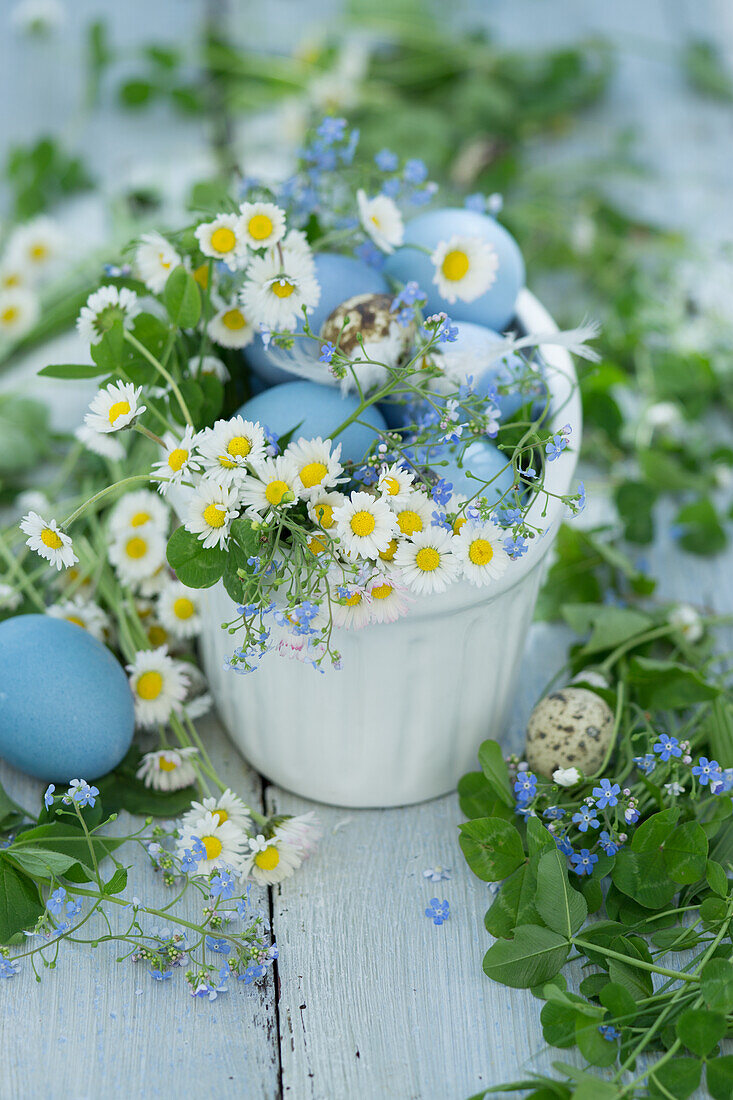 Schale gefüllt mit Ostereiern, Gänseblümchen und Vergissmeinnicht