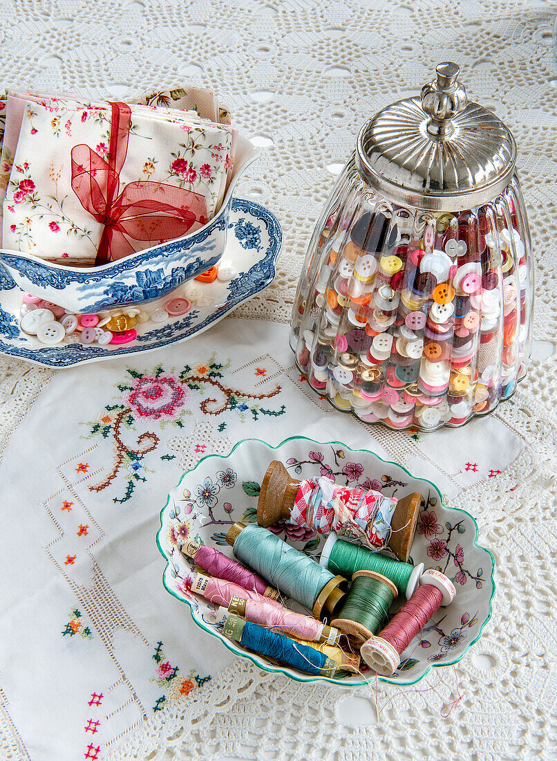 Nähzubehör: Knöpfe im Glas, Garnrollen, Stoff und Stickerei auf Häkeldecke