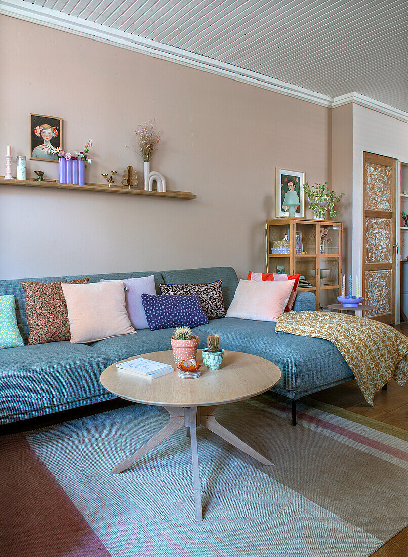 Wohnzimmer mit blauem Sofa, bunten Kissen und Holztisch auf Teppich