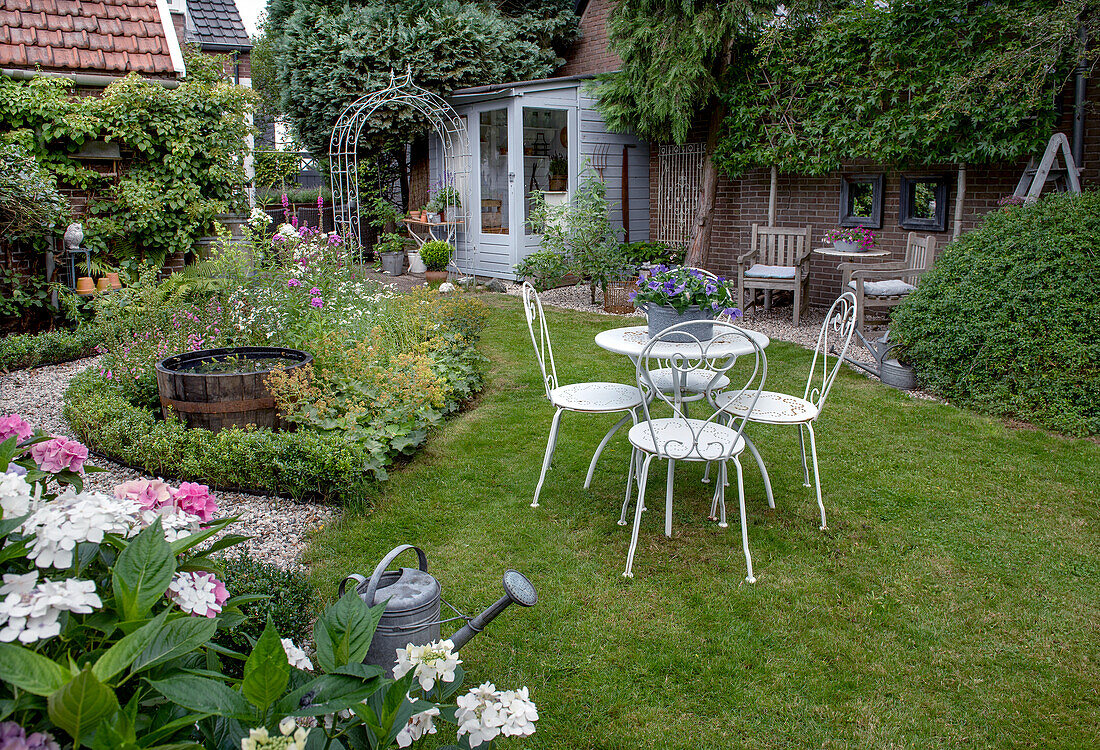 Ornamental garden with white metal table and matching chairs in summer