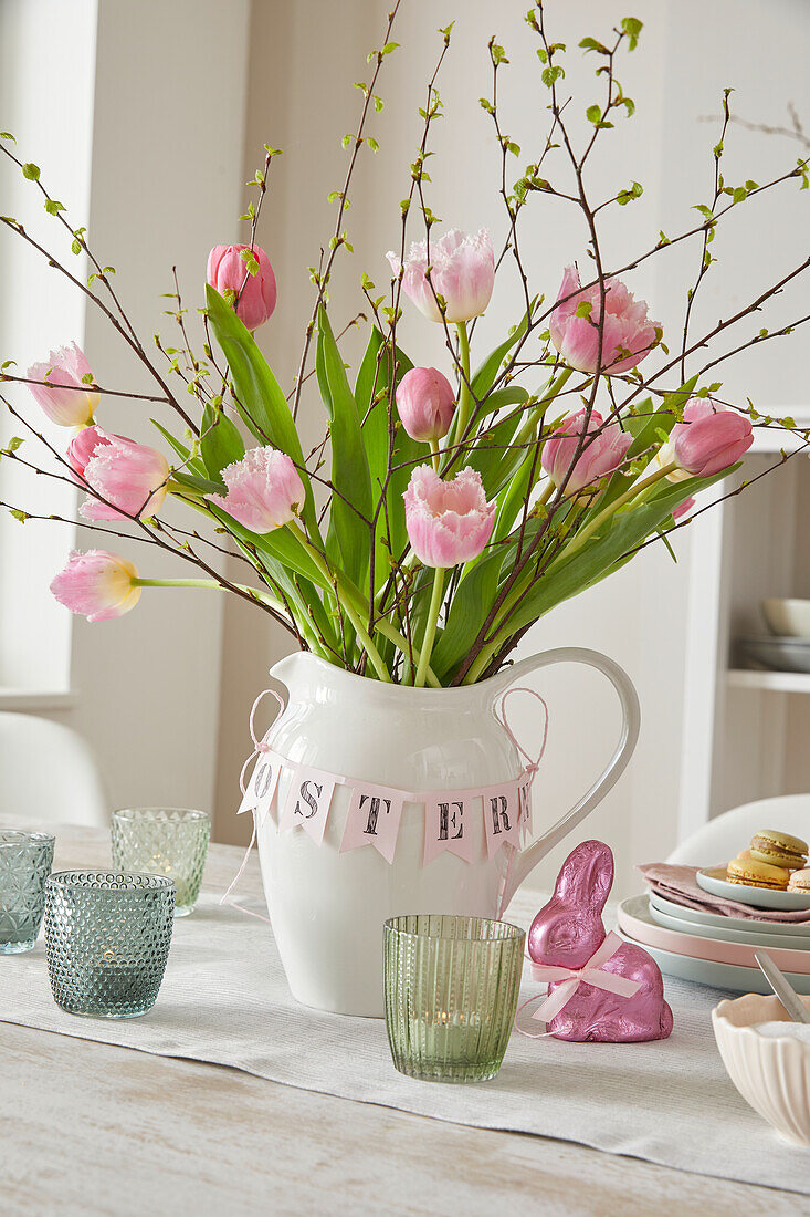 Rosa Tulpen (Tulipa) im weißen Krug mit Osterdeko auf gedecktem Tisch