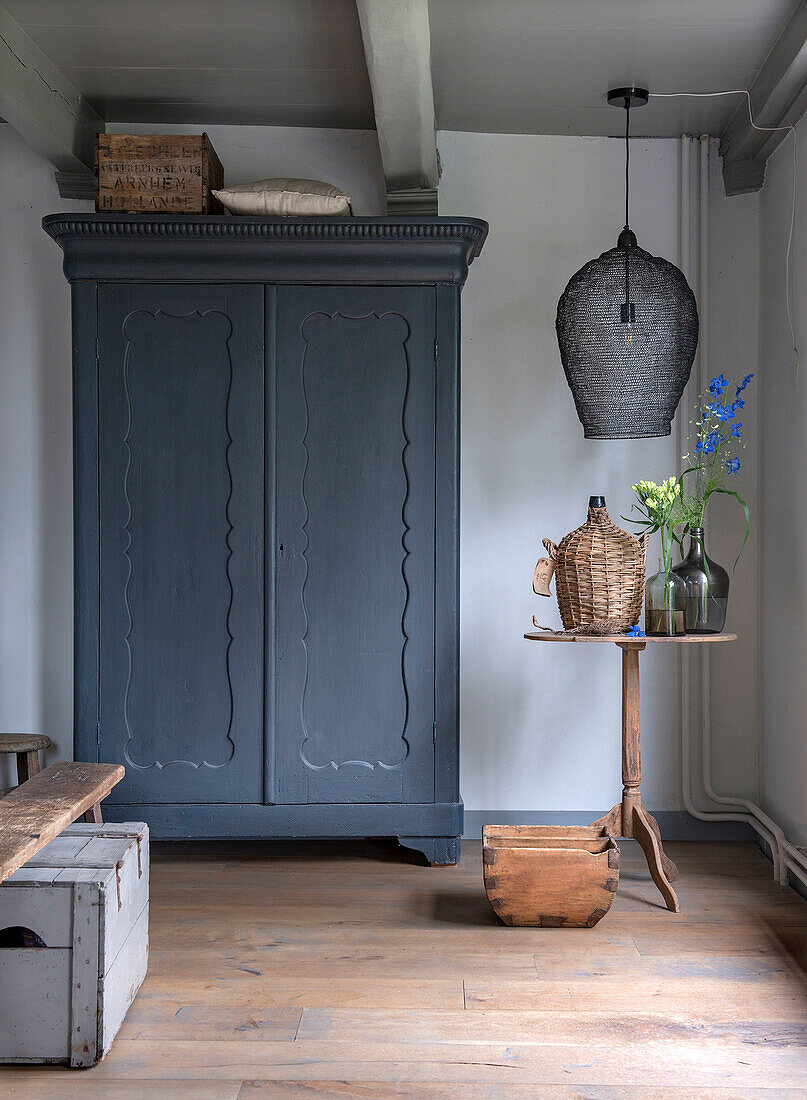 Blue-grey farmhouse cupboard and small side table with flower vases in rustic bedroom