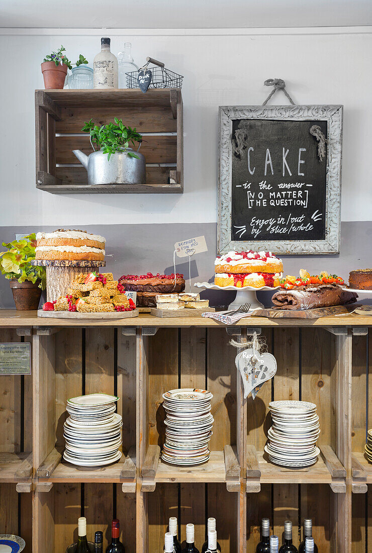 Cake counter with various cakes and pastries in front of a rustic wooden shelf