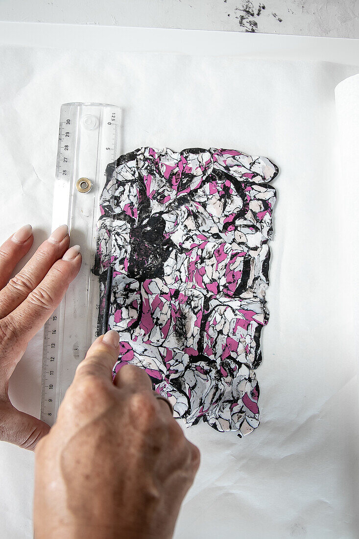 Man measures artistic collage of marbled clay with ruler