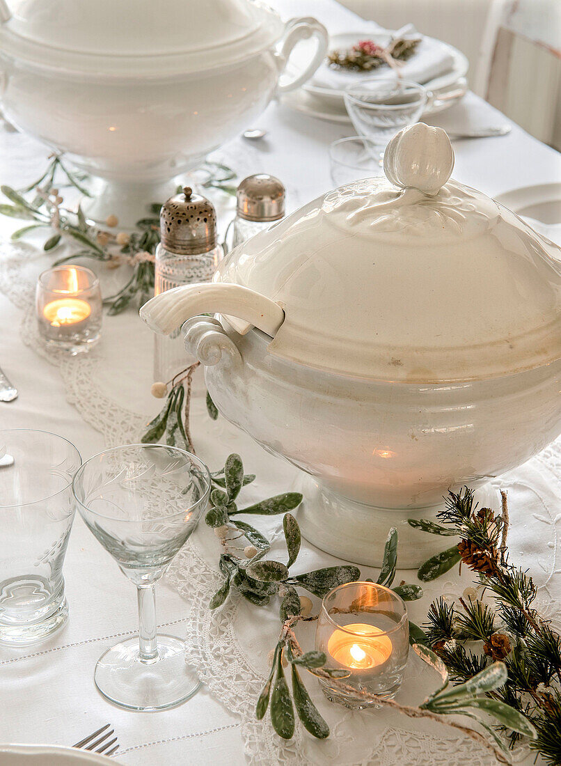 Christmas table setting in white, garland and soup tureen in the centre