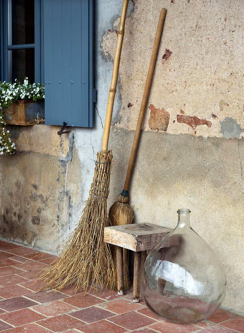 Broom and balloon bottle on terracotta tiled floor next to window with blue shutter