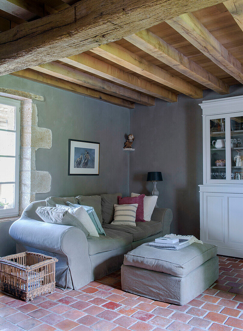 Cozy sofa and ottoman in living room with exposed beams and tiled floor