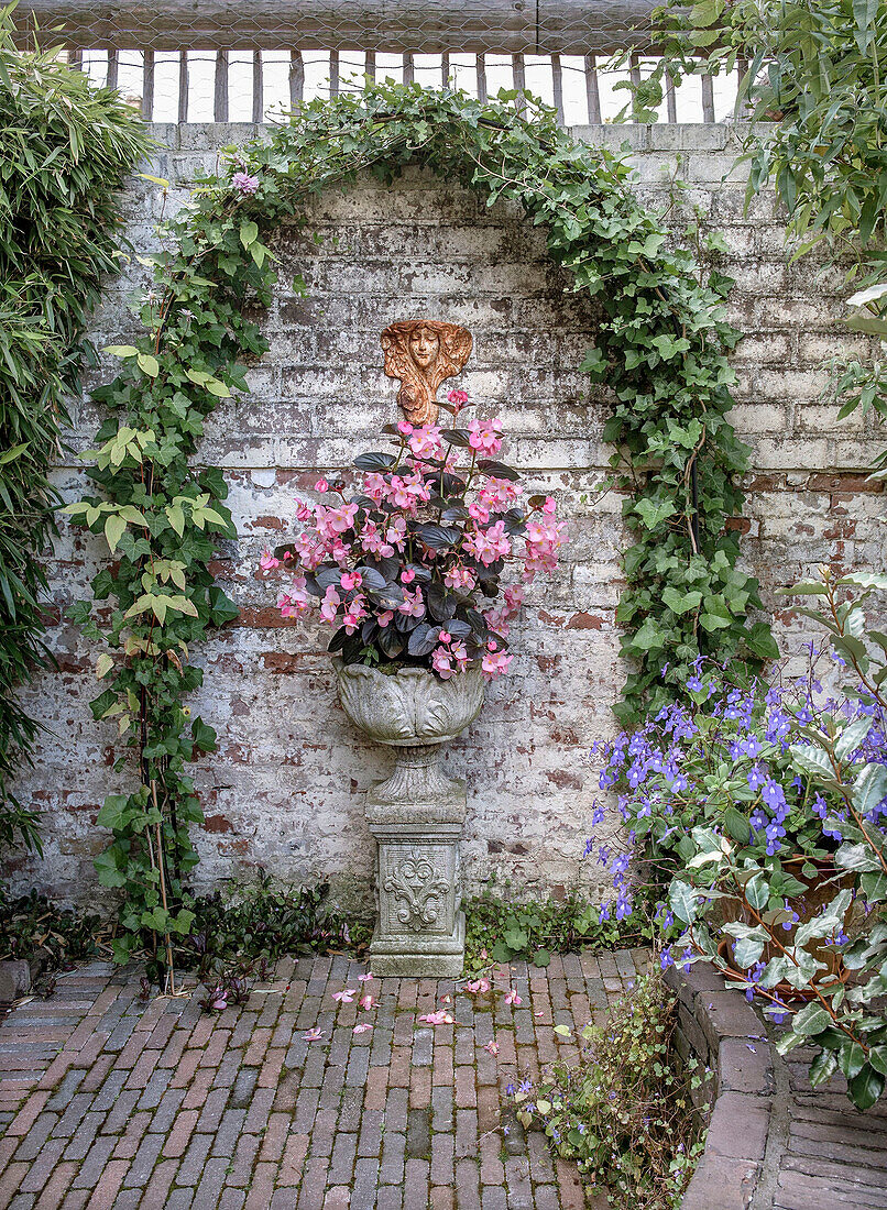 Blumenskulptur unter Efeu-Bogen vor Backstein-Gartenwand