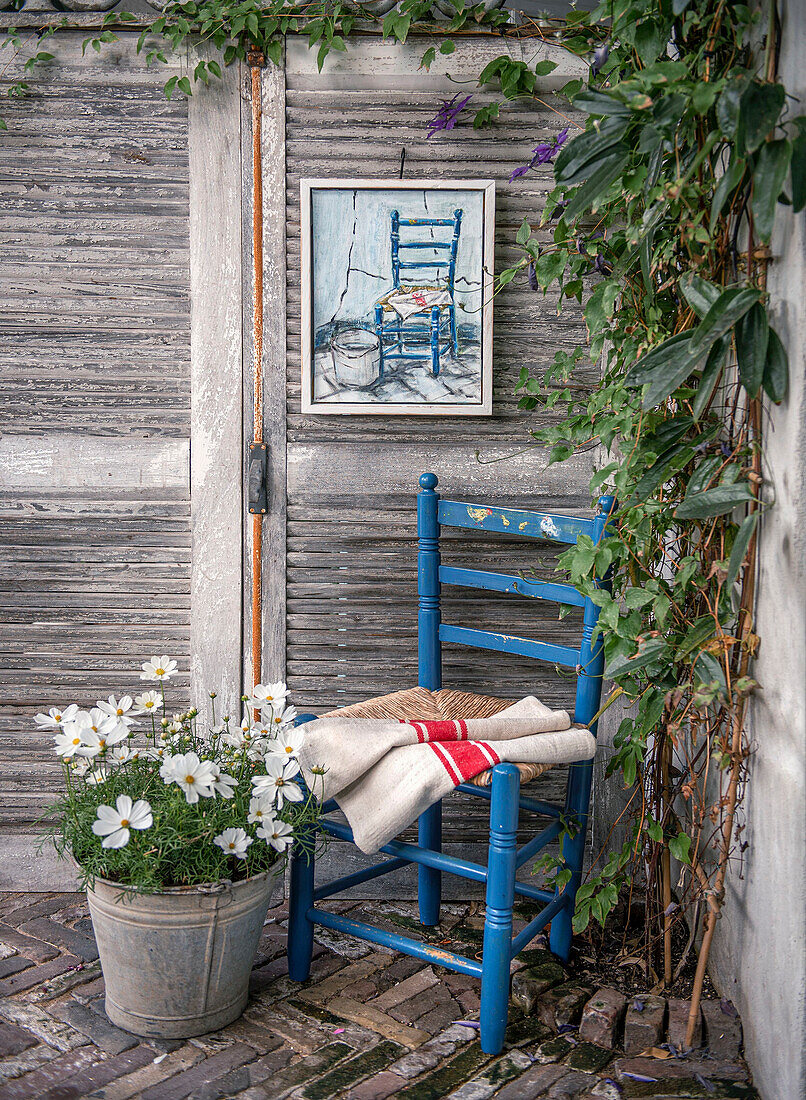 Blauer Holzstuhl und Metall-Blumentopf vor verwitterter Holzwand