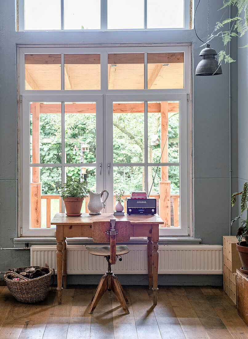 Antique wooden desk with potted plant, large window with view of greenery