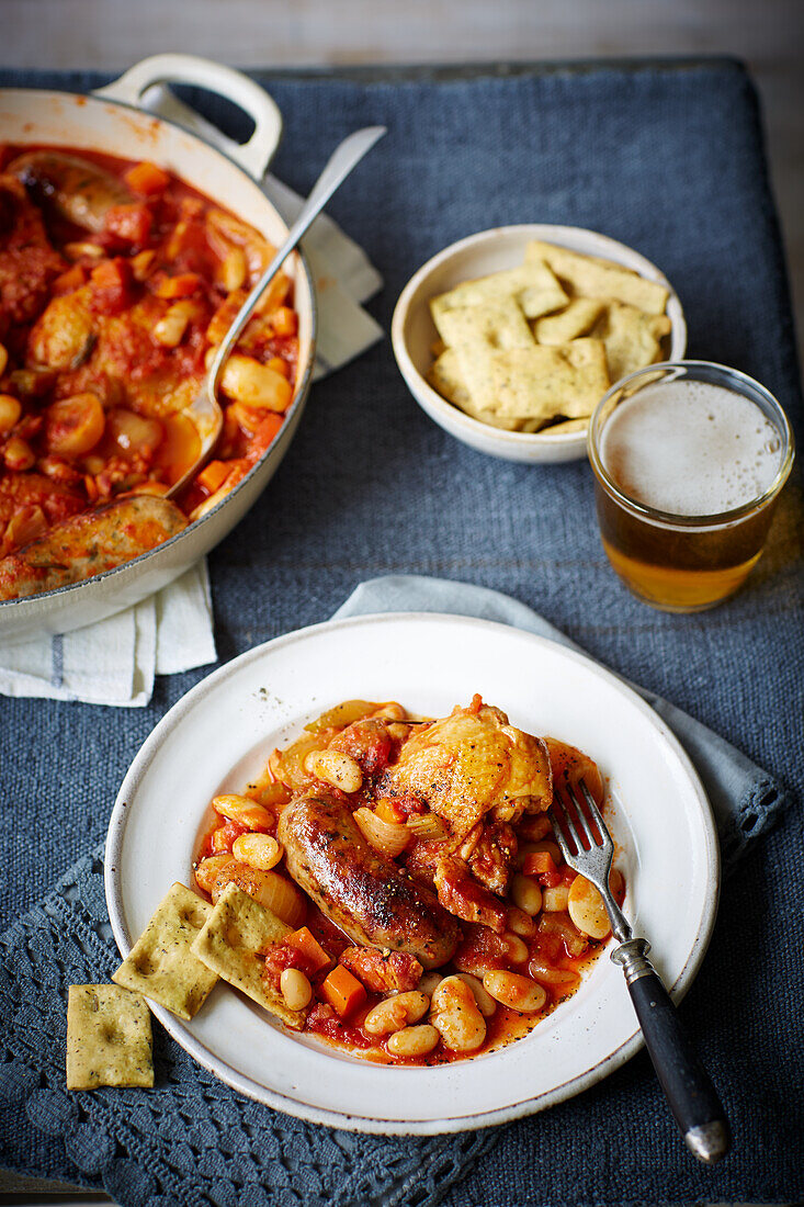 Hot pot with chicken, sausage, white beans, tomatoes, served with beer and crackers