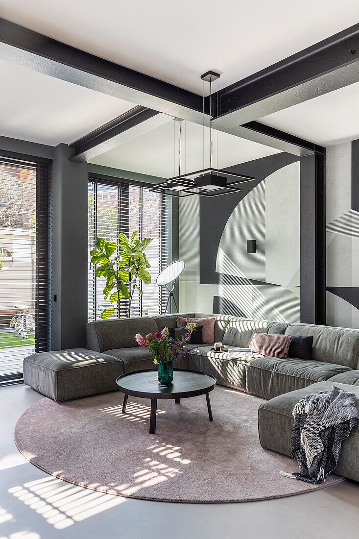 Modern living room with grey corner sofa, geometric wall design and pink carpet