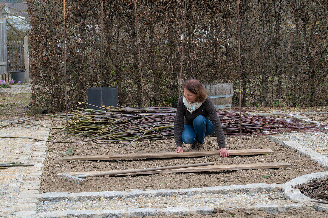 Frau bei Anlage eines Gemüsebeets mit Holzbrettern und einer Flechtwand aus Weidenzweigen für Kletterpflanzen