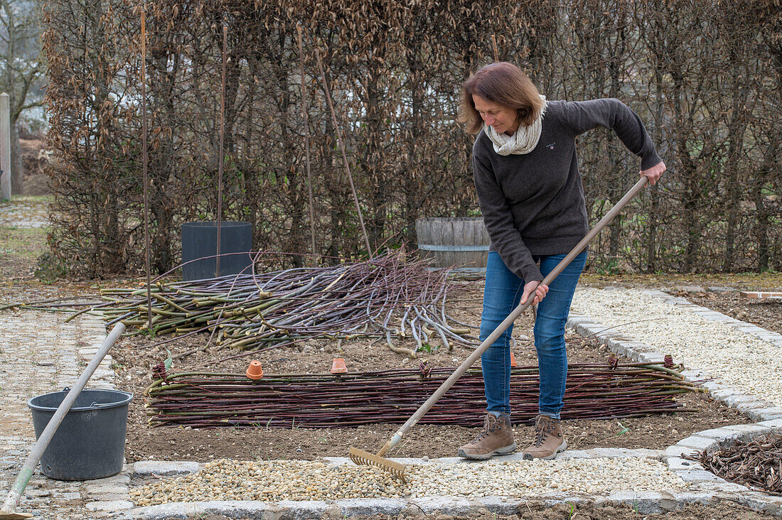 Frau bei Anlegen eines Gemüsebeets mit Flechtwand aus Zweigen und Weg anlegen mit Kies