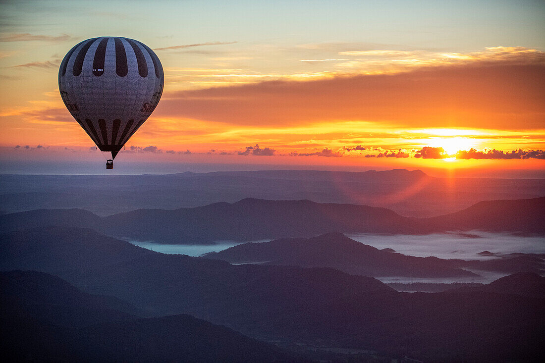Hot air balloon flying over mountains at sunset
