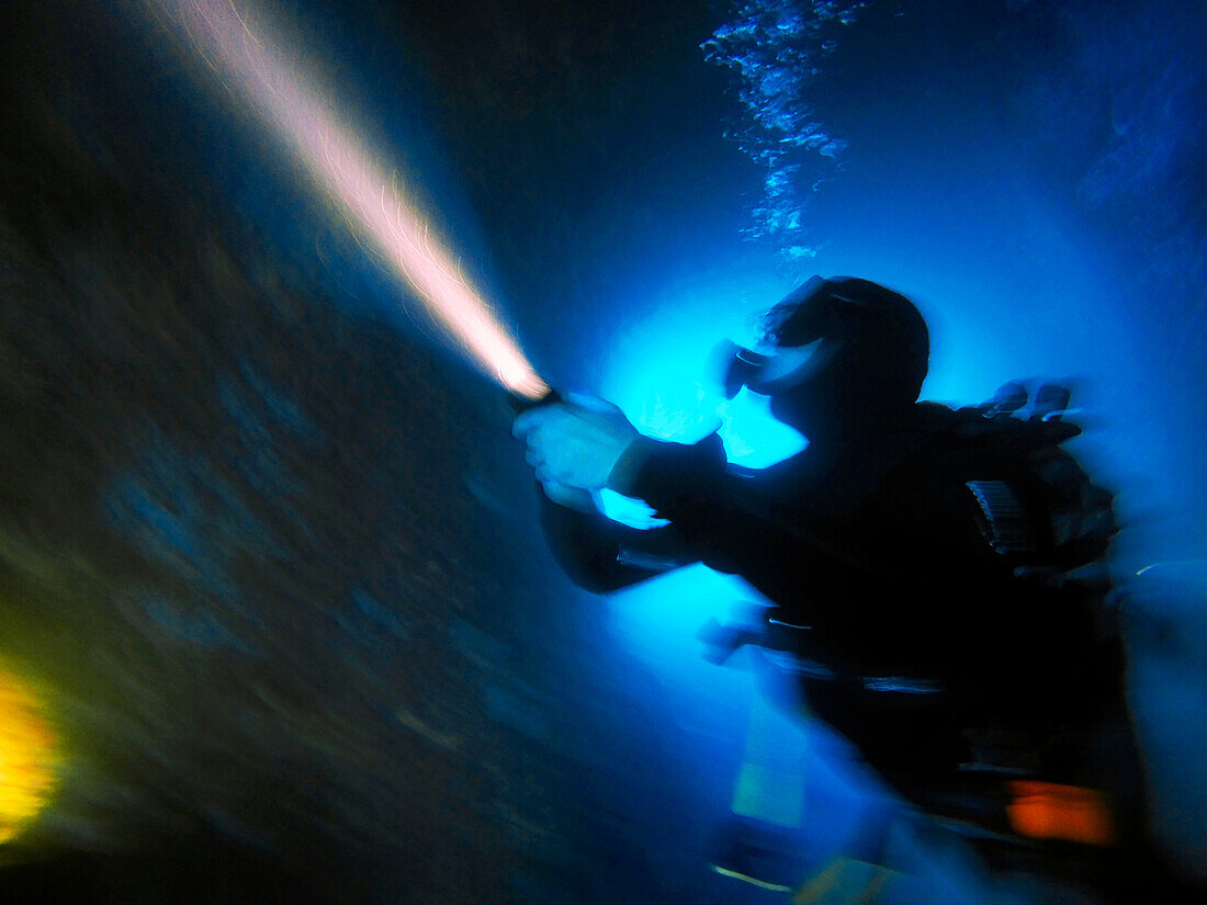 Scuba diver shining torch in underwater cave