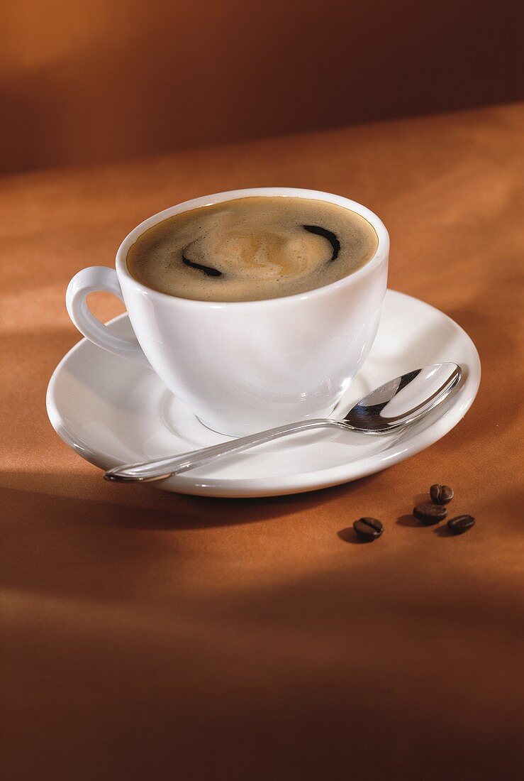 Eine Tasse Kaffee mit Löffel, daneben ein paar Kaffeebohnen