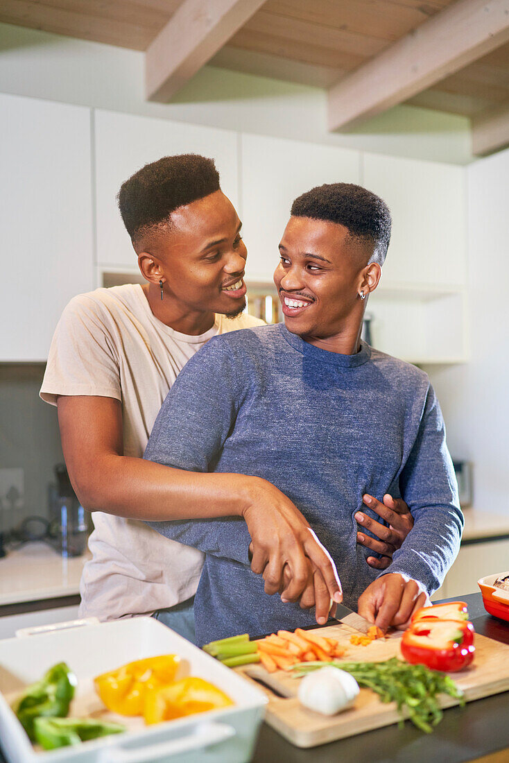 Happy young gay male couple cooking and hugging