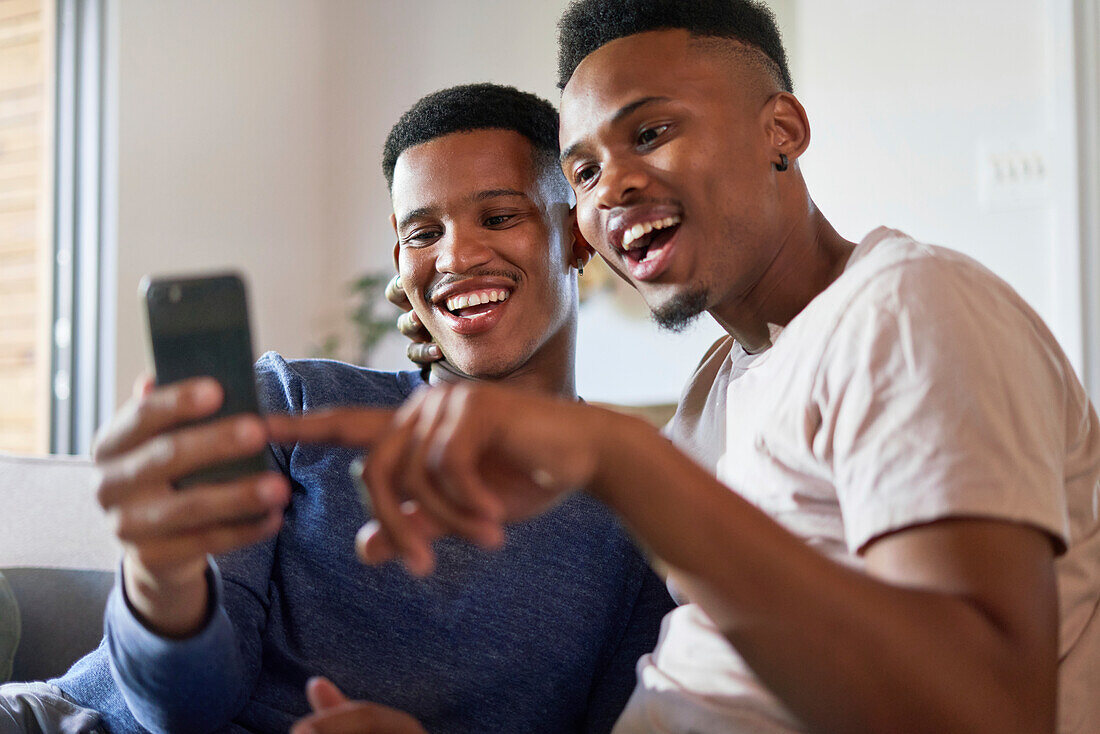 Happy young gay male couple using smart phone