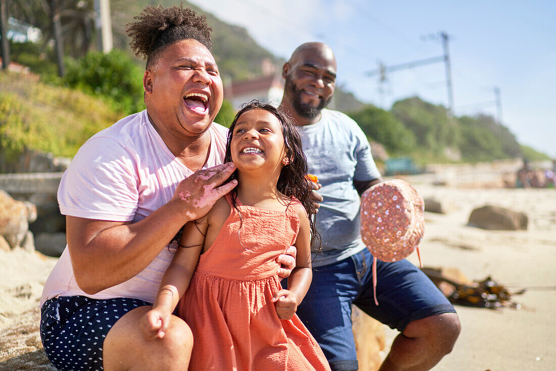 Happy gay male couple laughing on beach with daughter
