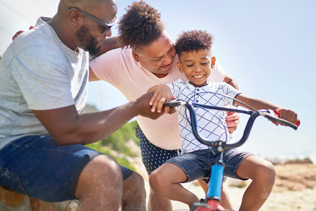 Happy gay male couple helping son ride a bike