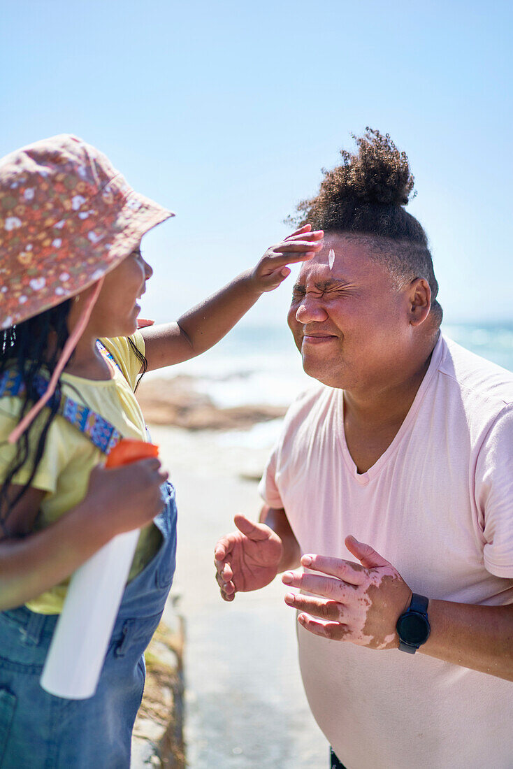 Daughter applying sunscreen to face of father on beach