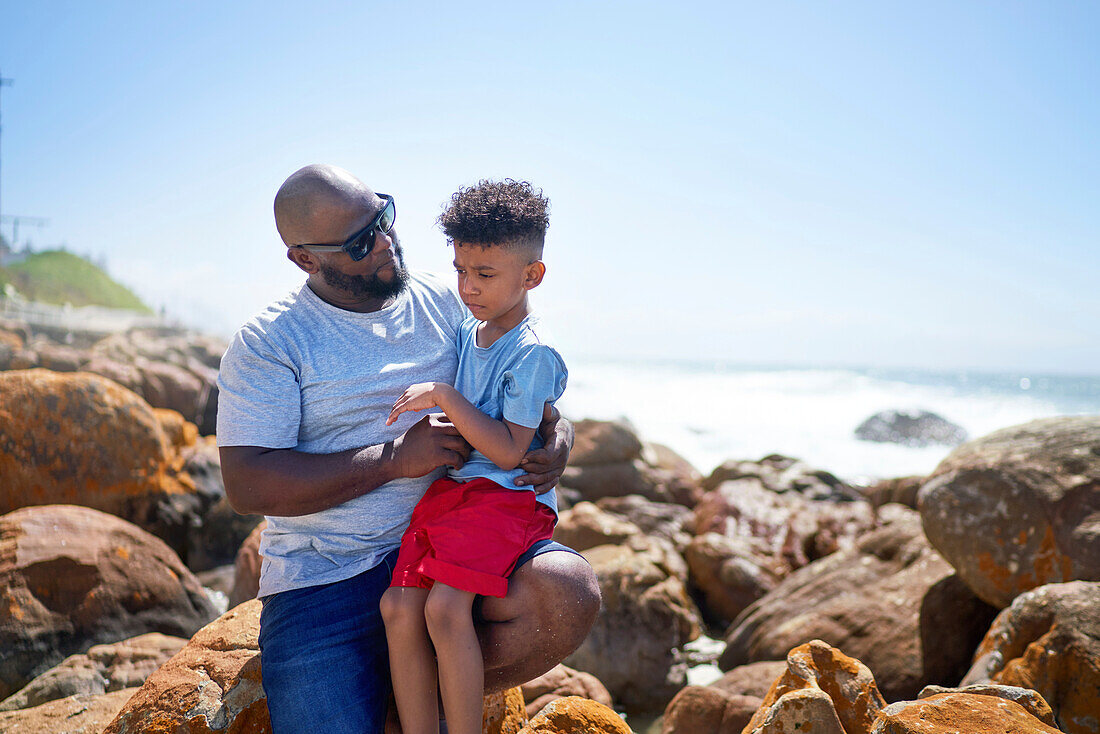 Affectionate father holding son on seaside rocks