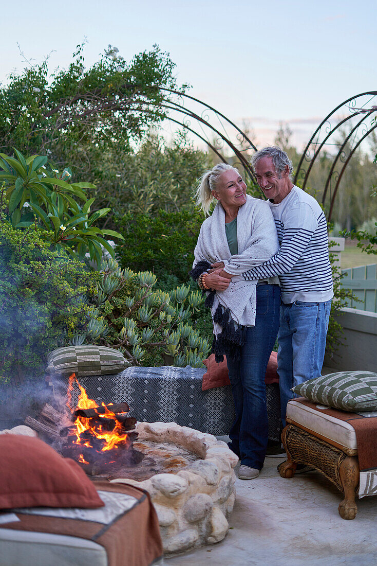 Senior couple hugging by fire pit on garden patio