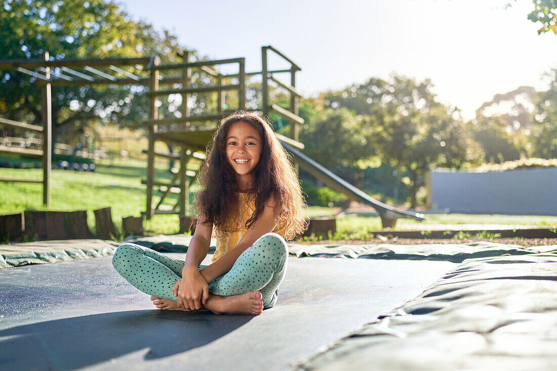 Girl sitting on trampoline in sunny backyard