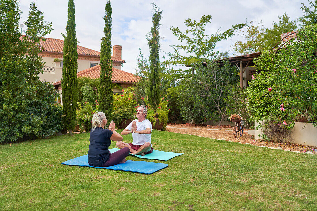 Serene senior couple meditating in summer villa garden